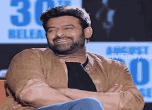 a man with a beard is smiling with his arms crossed while sitting down .