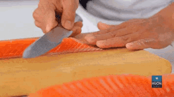 a person is cutting a piece of salmon on a wooden cutting board .