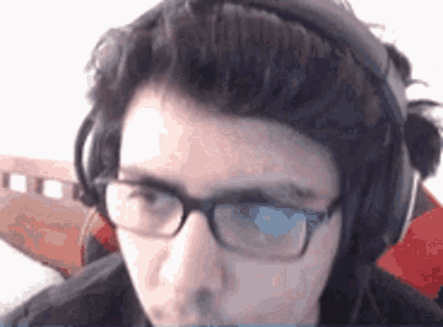 a young man wearing headphones and glasses is looking at the camera .