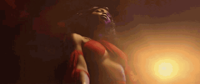 a woman in a red bra is dancing in a dark room with a light behind her .