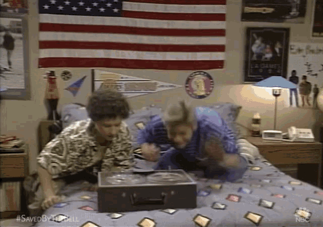 two people are laying on a bed with an american flag hanging on the wall .