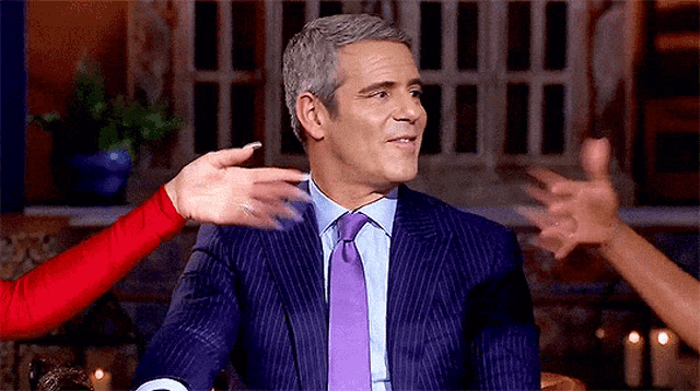 a man in a suit and tie is being touched by a woman 's hands .