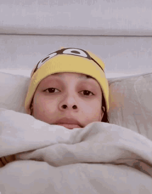 a woman is laying in bed with her eyes closed and a pink blanket covering her face .