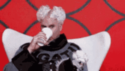 a man is sitting in a chair drinking a cup of coffee .