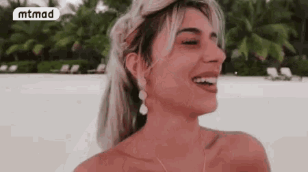 a woman is laughing on the beach while wearing earrings and a braided headband .