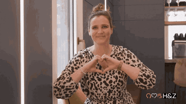 a woman in a leopard print dress is making a heart with her hands