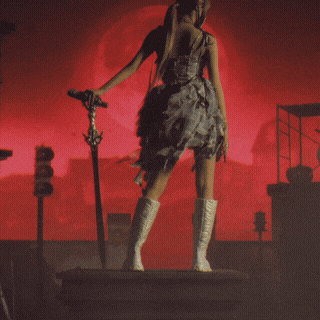 a woman in a plaid dress and white boots stands in front of a red background holding a microphone