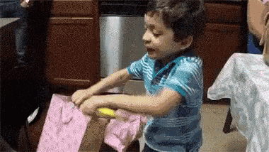 a little boy is opening a pink gift bag with a yellow object .