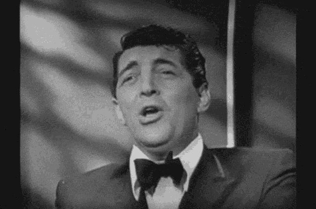 a black and white photo of a man in a tuxedo singing .