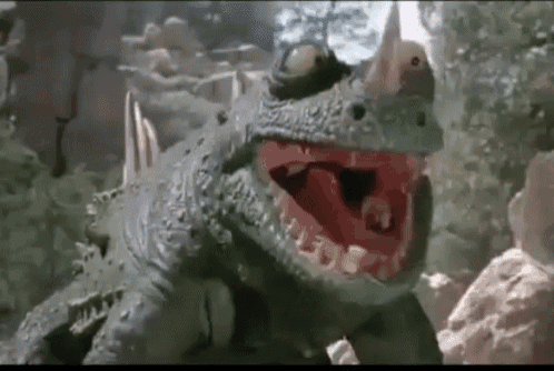 a dinosaur with its mouth open is standing on a rock in the woods .