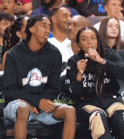 a man and a woman are sitting in a crowd wearing hoodies that say all dream team
