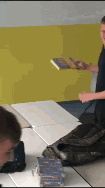 a boy is sitting at a table holding a book in his hand