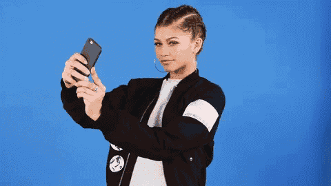 a woman wearing a black jacket is taking a selfie with her phone .