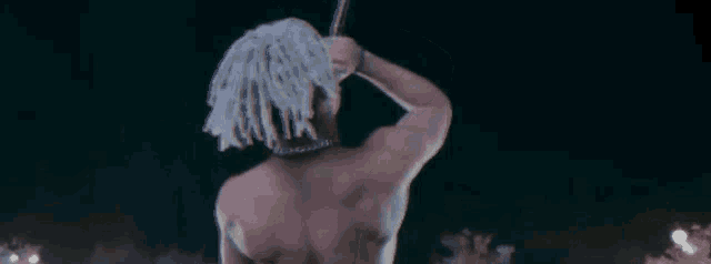 a shirtless man with white dreadlocks is standing in front of a crowd .