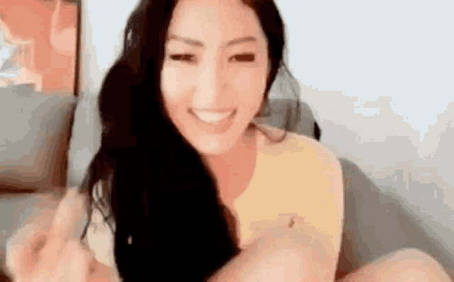 a woman is sitting on a couch smiling and making a heart shape with her hands .
