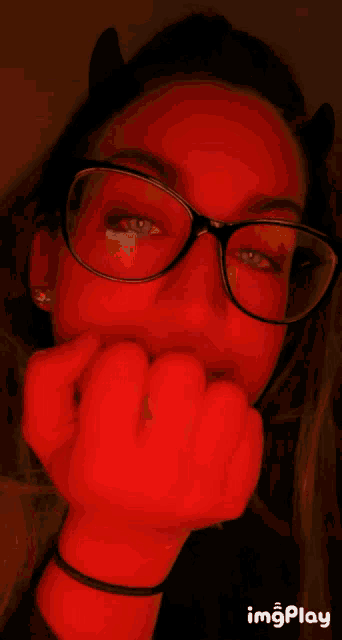 a girl wearing red glasses and devil horns has her hand on her face