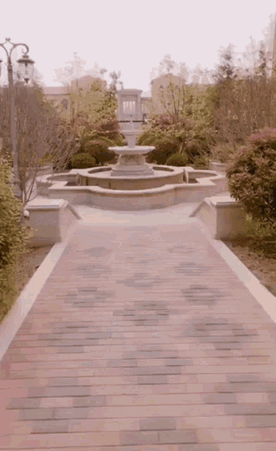 a brick walkway leads to a fountain in a garden