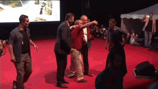 a group of men are standing on a red carpet and one of them is wearing a red shirt that says aa