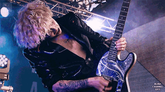 a man in a black leather jacket is playing a guitar on stage .