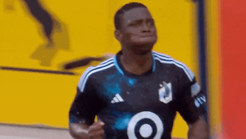 a soccer player wearing a black shirt with a white target on the front is running on the field .