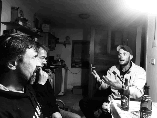 three men are sitting around a table with a bottle of gasser beer on it