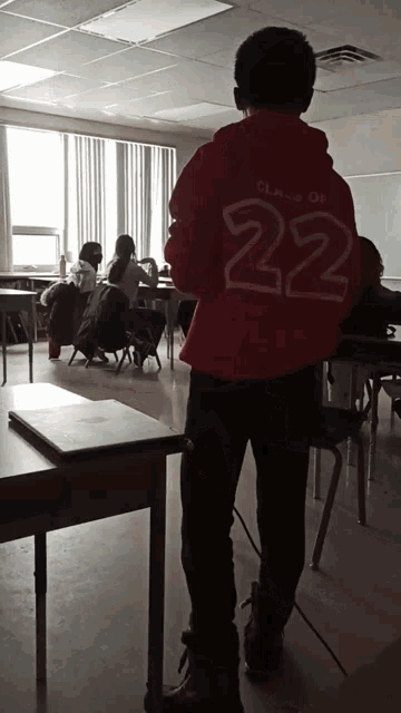 a boy wearing a red hoodie with the number 22 on it stands in a classroom