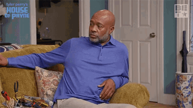 a man in a blue shirt is sitting on a couch with a house of payne logo behind him