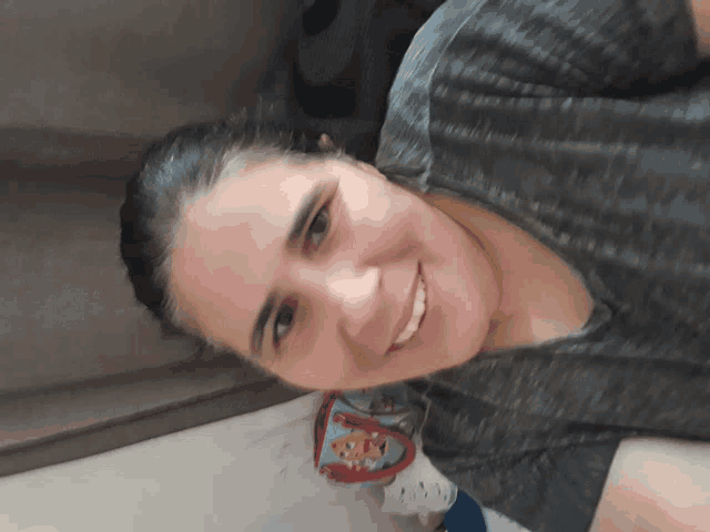 a woman wearing a grey shirt is smiling and looking at the camera