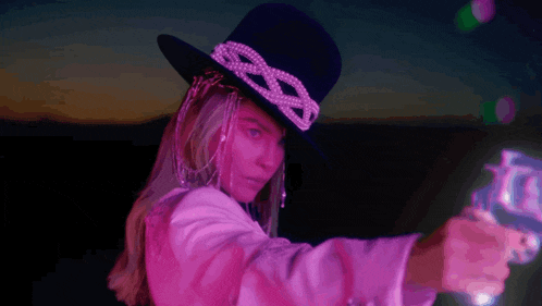 a woman in a cowboy hat holds a gun in her hand