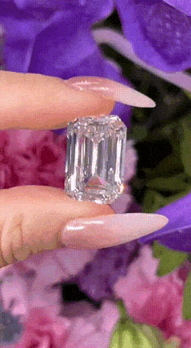 a woman with long nails is holding an emerald cut diamond in her hands