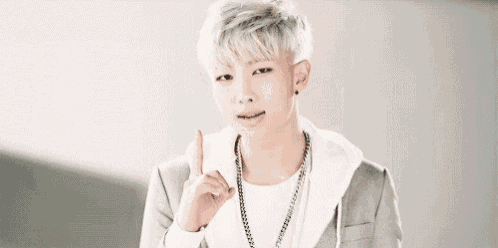 a young man with white hair and a necklace is giving a thumbs up sign .