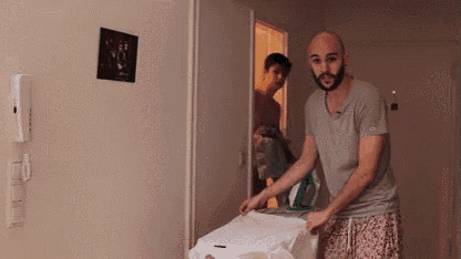 a man with a beard is ironing clothes in a room .