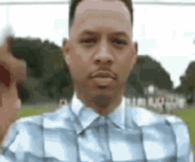 a man in a blue plaid shirt is taking a selfie with his phone .