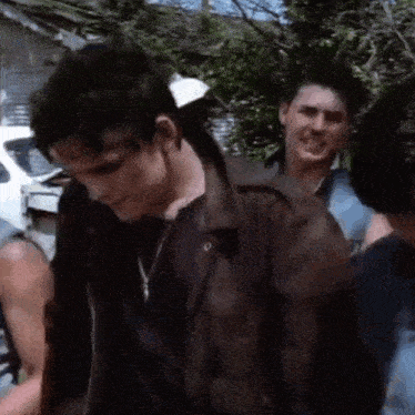 a man in a brown leather jacket is standing next to a group of people .