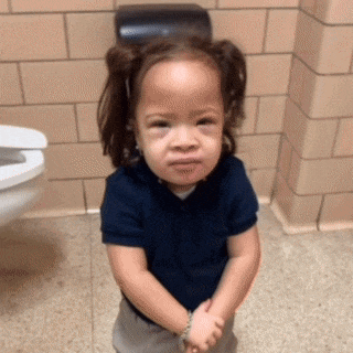 a little girl is standing in front of a toilet with her hands folded