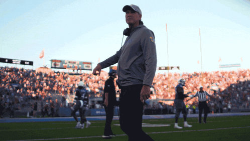 a man walking on a football field with a scoreboard in the background that says ' denver ' on it