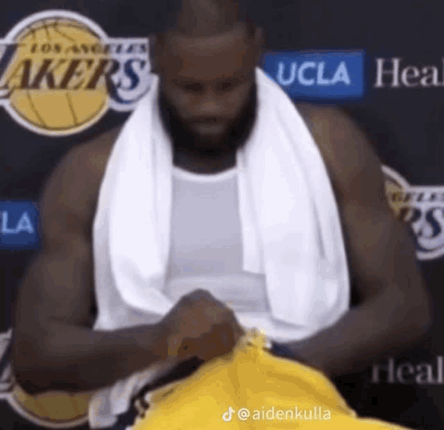 a basketball player with a towel around his neck is sitting in front of a lakers sign .