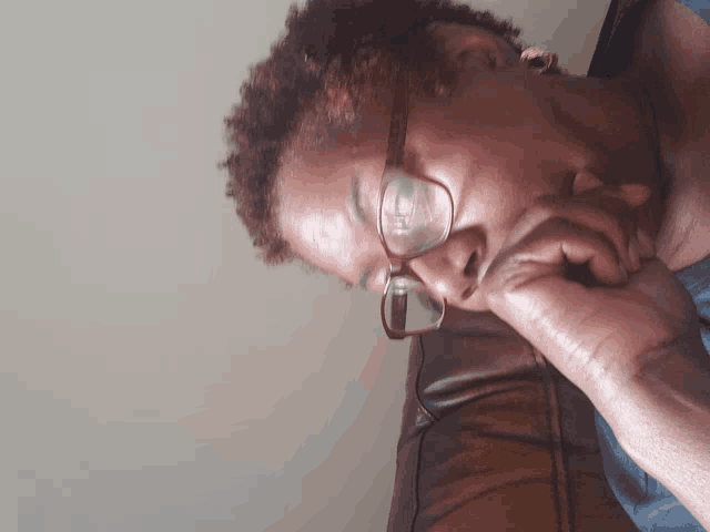 a woman wearing glasses is sitting on a couch with her hand on her chin