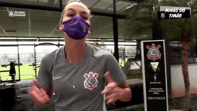 a woman wearing a purple face mask stands in front of a minas do timão sign