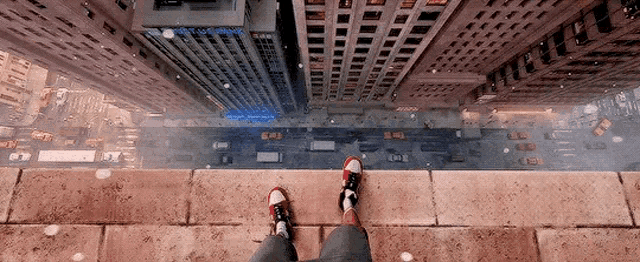 a person is standing on the edge of a building looking down at the city