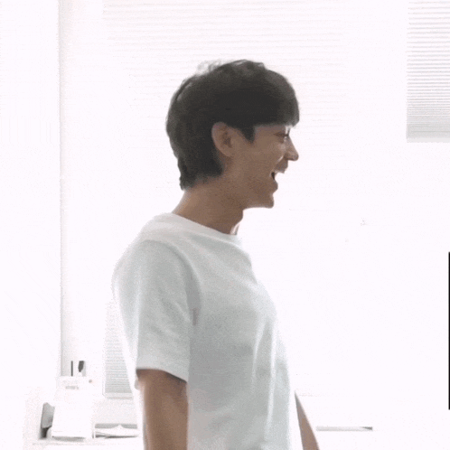 a man in a white t-shirt is standing in front of a window