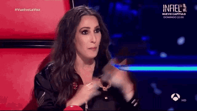 a woman is sitting in a chair on a stage and clapping her hands while wearing a black jacket .