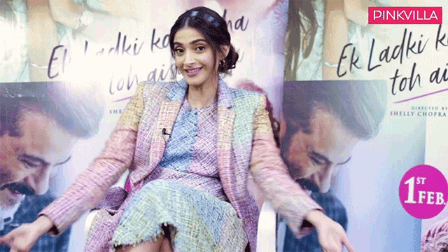 a woman is sitting in front of a pinkvilla sign