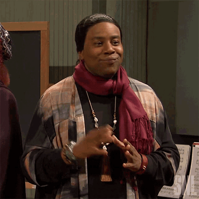 a woman wearing a scarf and a necklace is standing in front of a sign that says snl