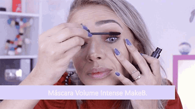 a woman with purple nails is applying mascara on her eyes