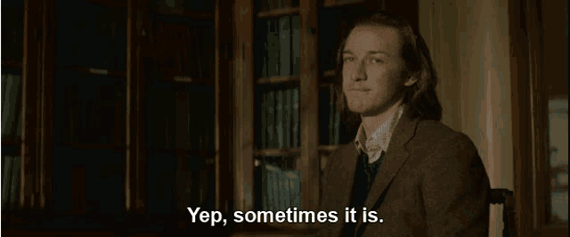 a man in a suit says yep sometimes it is in front of a bookshelf