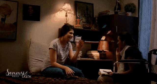 two women are sitting on a bed in a room with the word summer on the bottom right