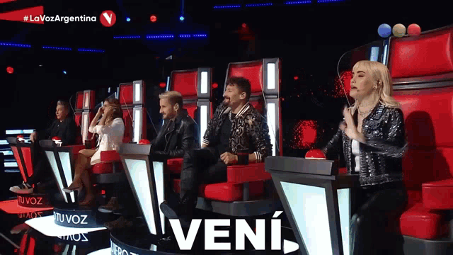 a group of people sitting in red chairs with the word veni on the bottom right