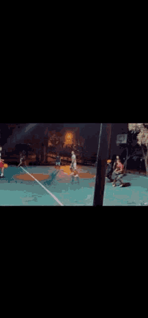 a group of young men are playing basketball on a court at night .