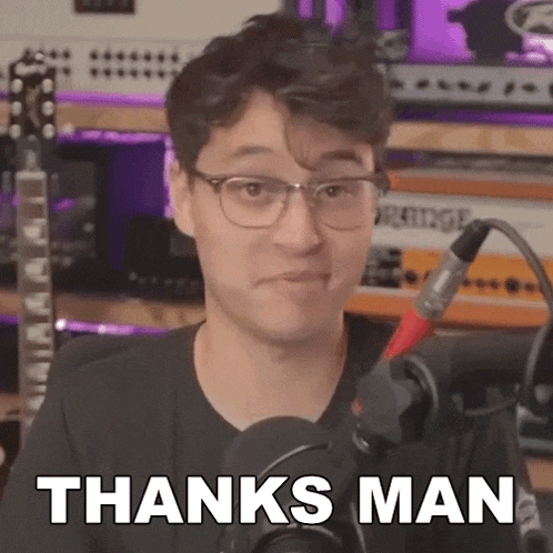 a man wearing glasses is standing in front of a microphone with the words `` thanks man '' written on it .